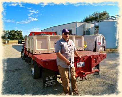 Man standing next to a red Lodi Winegrape Commission truck in a vineyard setting.