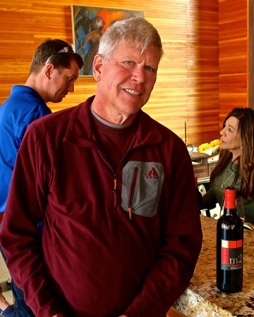 Smiling man at Lodi Winegrape Commission event with wine bottle on bar.