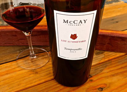 Bottle of McCay Cellars Tempranillo wine with glass of red wine on wooden table.