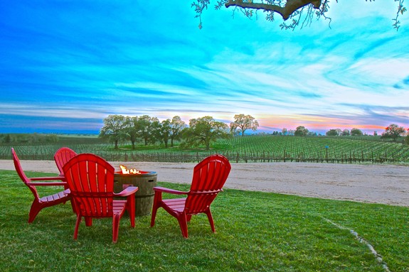 Red Adirondack chairs and fire pit overlooking a vineyard at sunset in Lodi, California.