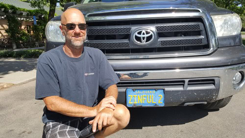 Man with sunglasses kneeling in front of a Toyota truck with ZINFUL 2 license plate in Lodi, California.
