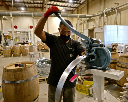 Winery worker using a saw to cut wine barrels at Lodi Winegrape Commission facility.