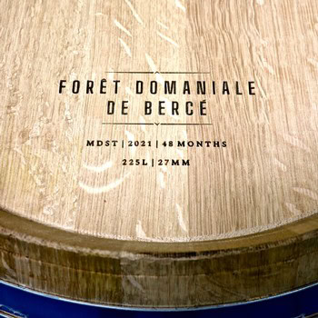 Close-up of a wine barrel with engraved text, used for aging wine in a forest domain in France.