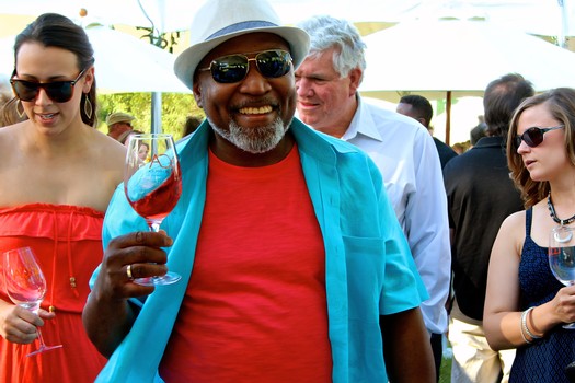 Smiling man with sunglasses holding a glass of rosé wine at a wine tasting event.