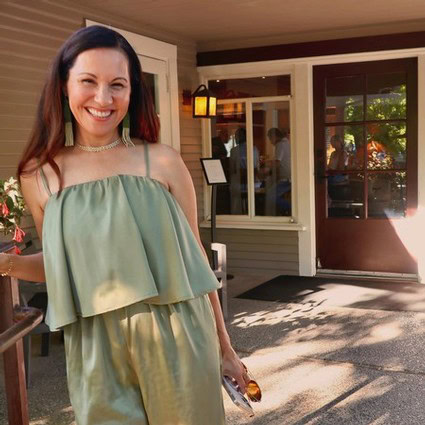 Smiling woman standing outside Lodi Winegrape Commission building in sunlight.