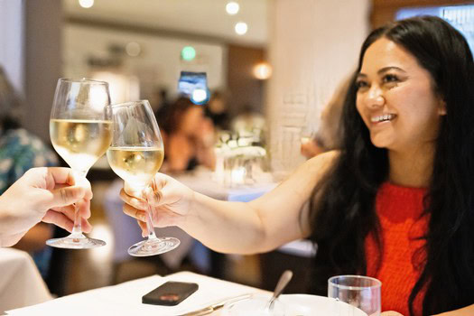 Woman toasting with white wine glasses at a social event in Lodi, California.