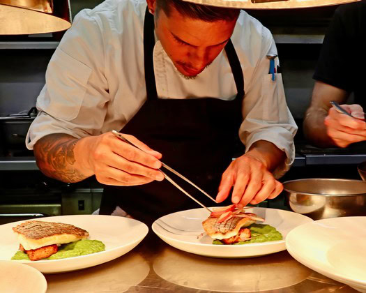 Chef preparing a gourmet dish with precision in a professional kitchen setting.