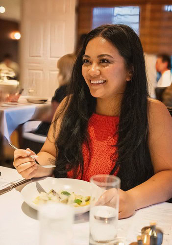 Smiling woman enjoying a meal at a Lodi Winegrape Commission event in a cozy restaurant setting.