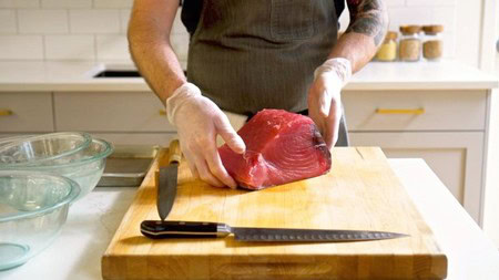 Person slicing fresh beef on a wooden cutting board in a modern kitchen.