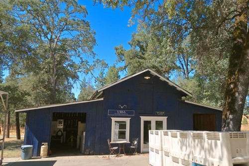 Blue building of Lodi Winegrape Commission surrounded by trees and outdoor equipment.