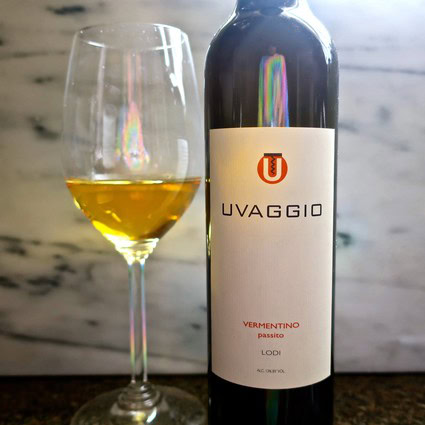 Bottle of Uvaggio Vermentino wine with a glass of wine beside it, on a rustic background.