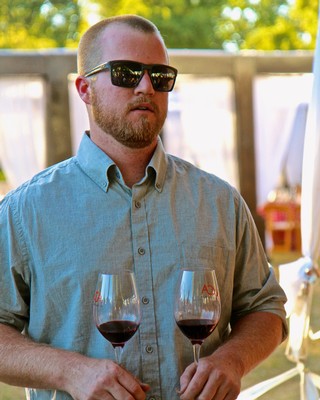 Man with sunglasses holding two glasses of red wine at a Lodi wine event.