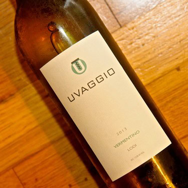 Close-up of a wine bottle labeled 'Uvaggio Vermentino 2015 Lodi' on a wooden surface.