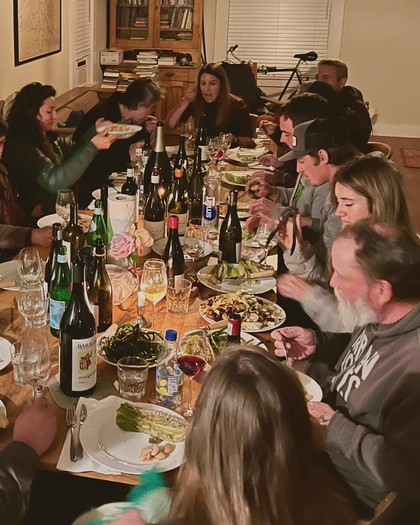 Group of people enjoying a dinner with wine bottles on a long table, in a cozy indoor setting.