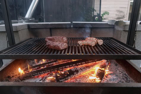 Steaks grilling on an outdoor barbecue grill with open flames, perfect for wine and food pairing events.