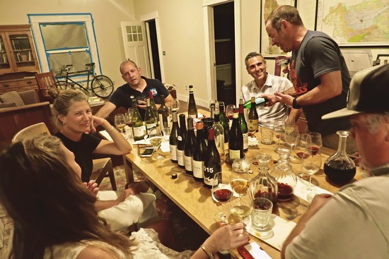 Group of people enjoying wine tasting at a dinner table with wine bottles and glasses.