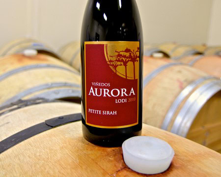 Lodi Aurora Petite Sirah wine bottle from 2010 on wine barrels at a winery.