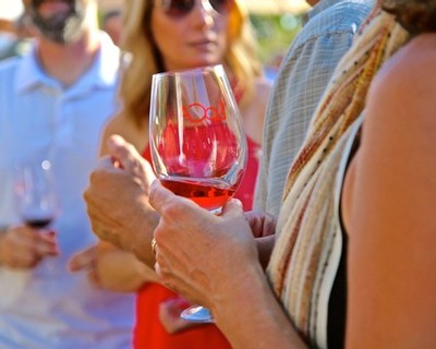People enjoying wine tasting outdoors, holding glasses of red wine, at a Lodi Winegrape Commission event.