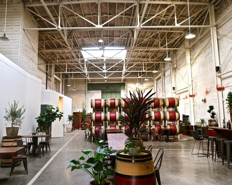 Interior view of a winery with wine barrels, plants, and seating area, showcasing Lodi Winegrape Commission's wine production.
