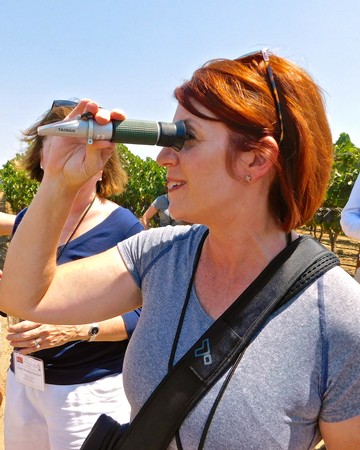 Woman using binoculars during Lodi Winegrape Commission vineyard tour in sunny outdoor setting.