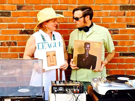 Two people with vinyl records and DJ equipment against a brick wall at Lodi Winegrape Commission event.