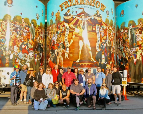 Group of people in front of a colorful circus-themed mural at Lodi Winegrape Commission event.