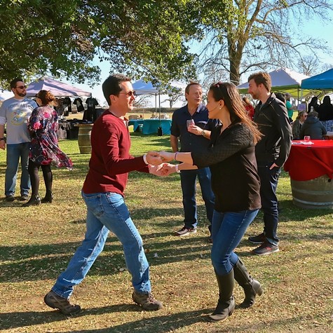 People dancing and socializing at an outdoor Lodi wine event with tents and trees in the background.