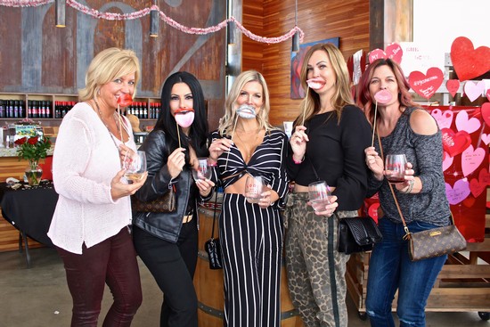 Group of women celebrating with wine and heart-shaped decorations at Lodi Winegrape Commission event.