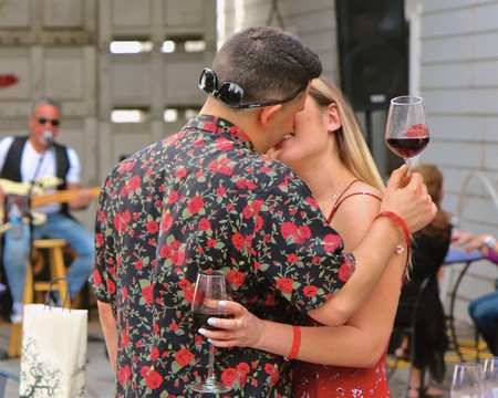 Couple sharing a kiss while holding glasses of red wine at Lodi Wine event.