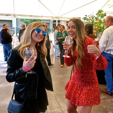 Two women enjoying wine at a Lodi Winegrape Commission event, smiling and holding wine glasses, with other attendees in the背景.