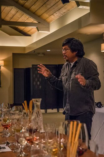 Man speaking at a wine tasting event with glasses of wine and tasting sticks on the table.