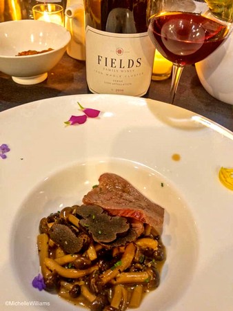 Wine and food pairing with a glass of red wine, wine bottle, and gourmet dish on a table.