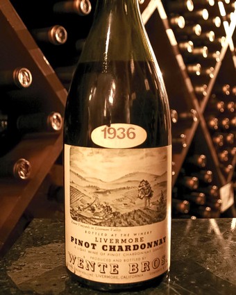 Old 1936 Livermore Pinot Chardonnay wine bottle with landscape label in wine cellar.
