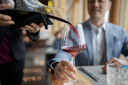 Person pouring red wine into a glass during a wine tasting event at Lodi Winegrape Commission.