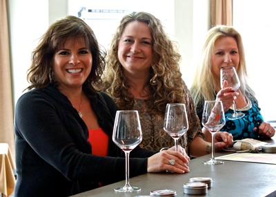 Women enjoying wine tasting at Lodi Winegrape Commission event with glasses of wine and smiling faces.