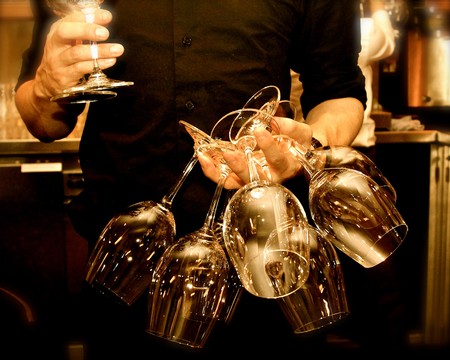 Person holding multiple wine glasses at a wine tasting event, showcasing wine glasses and a wine bar background.