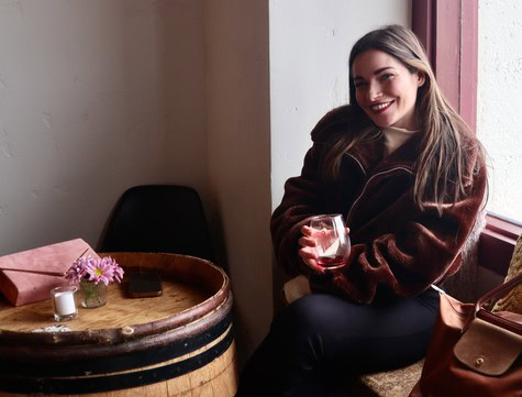 Young woman enjoying wine at a Lodi Winegrape Commission event, sitting by a window with a glass of wine.