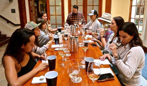 Group of people enjoying wine tasting at a Lodi Winegrape Commission event, with wine glasses and a tasting table.