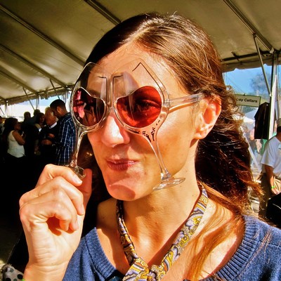 Woman tasting wine at Lodi Winegrape Commission event, wearing sunglasses and a blue top.
