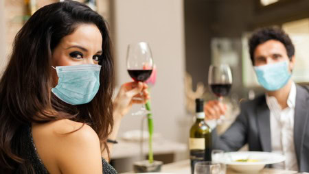Woman and man wearing masks enjoying wine at a social gathering.
