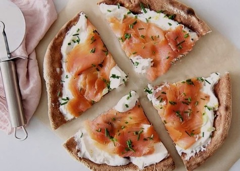 Delicious bagel pizza topped with smoked salmon, cream cheese, and chives, sliced into four pieces.