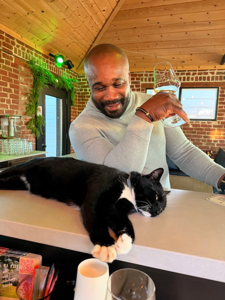 Man enjoying wine with a relaxed black and white cat at a winery.