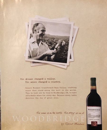 Vintage photo of man holding a grape cluster with a bottle of Woodbridge wine nearby.