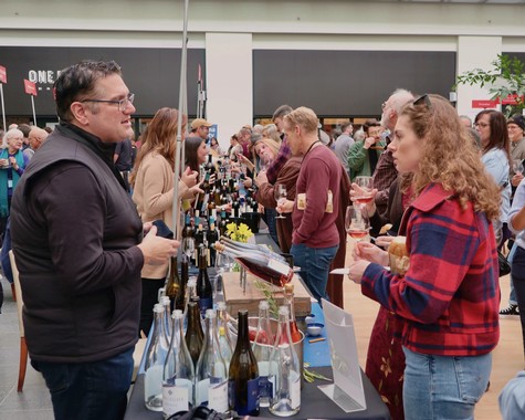People enjoying wine tasting at the Lodi Winegrape Commission event with bottles and glasses on display.