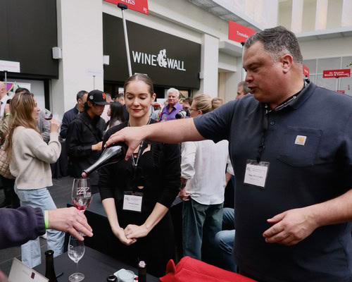 Man pouring wine at Lodi Winegrape Commission event with attendees in background.