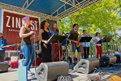 Live outdoor music performance at a Lodi Winegrape Commission event with musicians on stage and audience in a park setting.