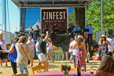 Lodi Winegrape Commission booth at Zinfest with live music and visitors enjoying outdoor event.