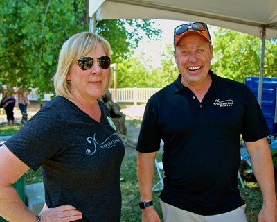 Two smiling individuals at a Lodi Winegrape Commission event outdoors, wearing branded shirts and sunglasses.