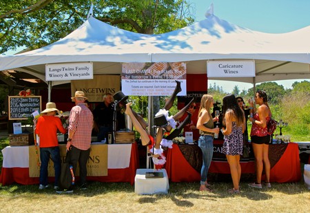 People enjoying wine tasting at the Lodi Winegrape Commission outdoor event under a white canopy tent.