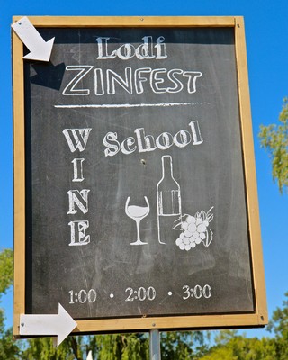 Chalkboard sign advertising Lodi ZinFest wine event with wine glass, bottle, and grapes illustrations.